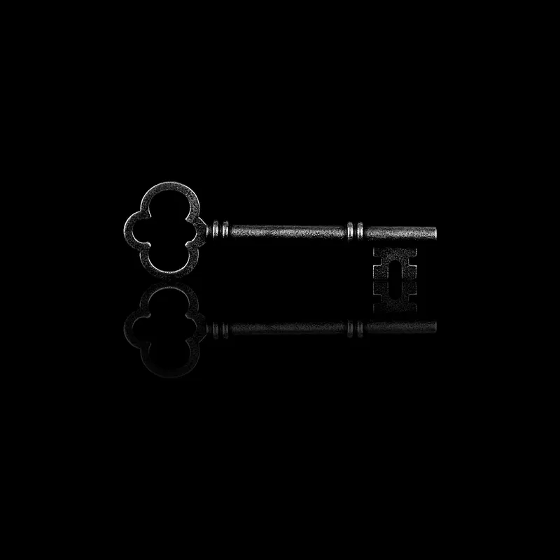 Clé ancienne en métal, posée sur un miroir noir qui la reflète
